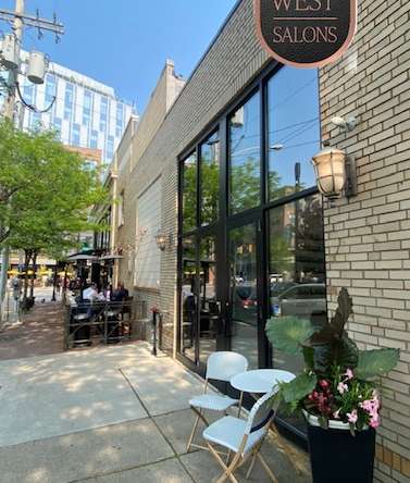 Modern salon exterior with outdoor seating and greenery in an urban shopping district.