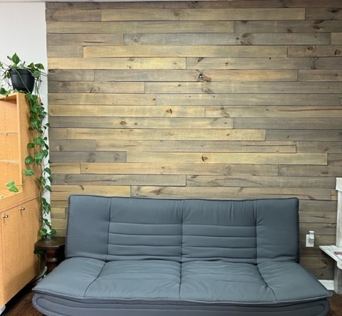 Comfortable gray sofa in a stylish salon lounge with wooden accent wall, perfect for clients waiting.