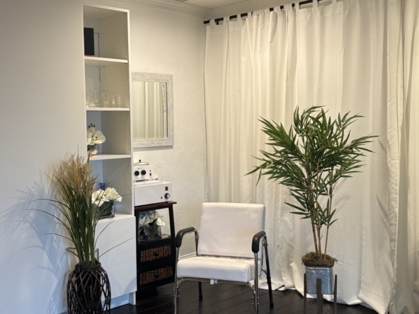 Clean, modern salon rental space with white curtains, a white chair, and tropical plants. Perfect for beauty professionals seeking a cozy, stylish environment.