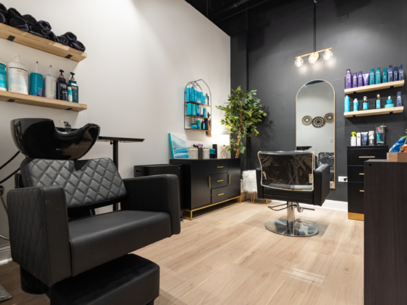 Stylish salon station with black styling chair and washbasin, modern decor, salon supplies and shelves.