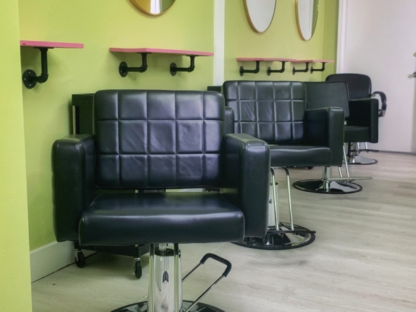 Black salon chairs in a modern hair salon with green walls and round mirrors.