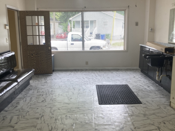 Empty salon interior with large front window, ceiling fan, and vinyl flooring—ideal for rent or salon setup.