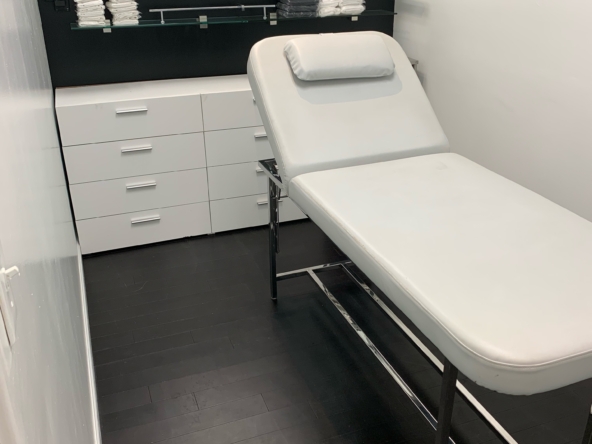 Private salon treatment room with adjustable massage bed, clean towels, and modern decor.