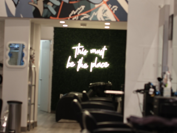 Stylish hair salon with black chairs, graffiti artwork, and a neon sign that says "This must be the place".