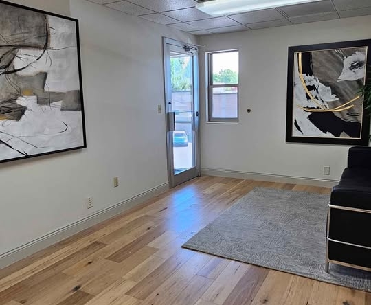 Bright, modern salon rental space with artwork, natural light, and hardwood flooring.