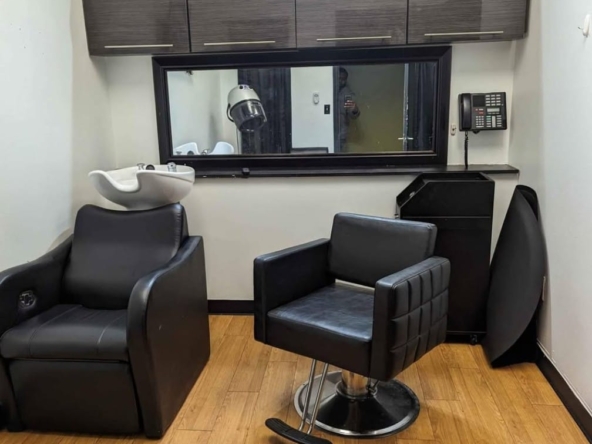 Clean salon station with black chairs, hair washing sink, mirror, and storage cabinets. Ideal for salon rentals and hairstyling.