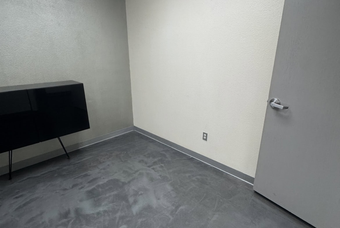 Empty salon room with gray flooring, ceiling tiles, door, and minimal decor.