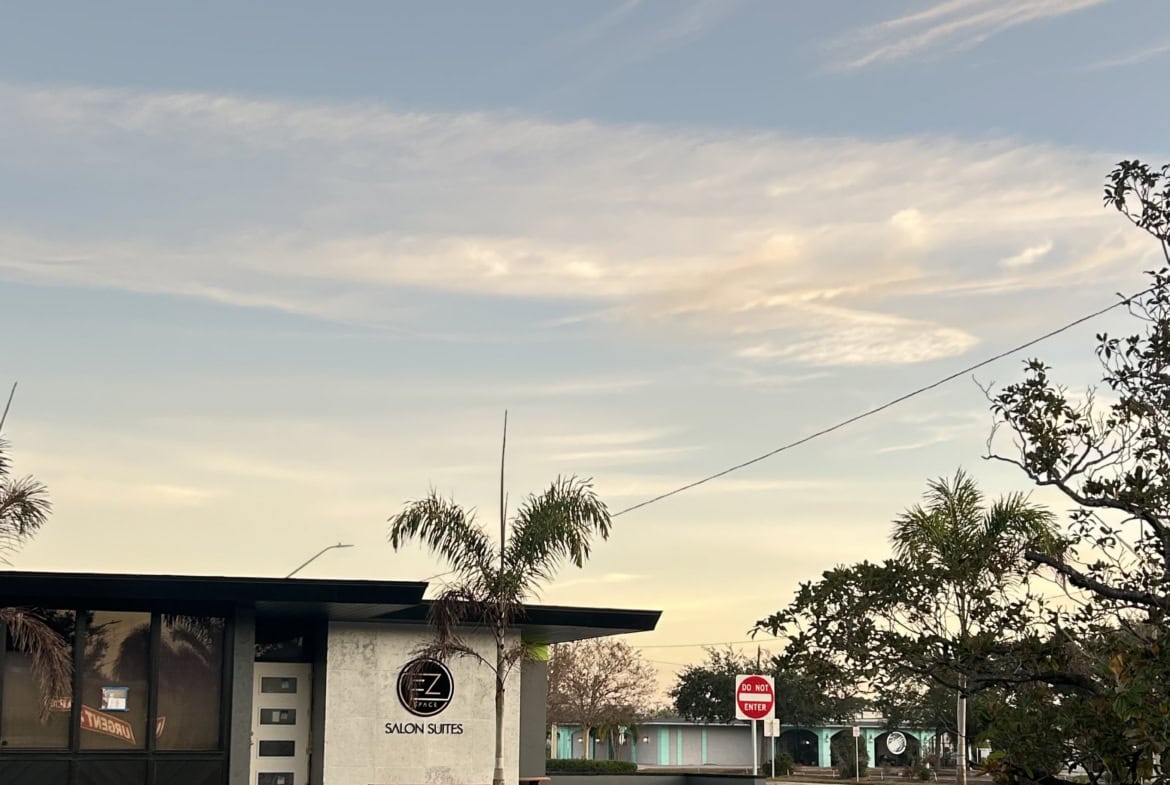 Modern salon suites building with palm trees and clear sky.