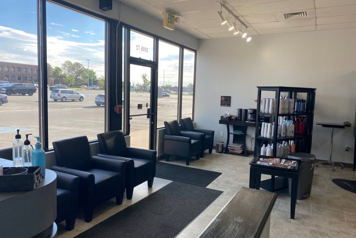 Contemporary salon waiting area with black chairs, large windows, and a bookshelf.