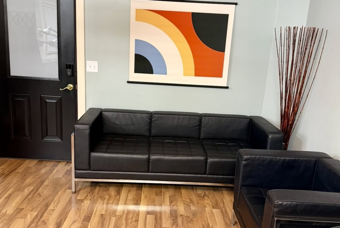 Waiting area with black leather sofa and vibrant abstract wall art in salon.