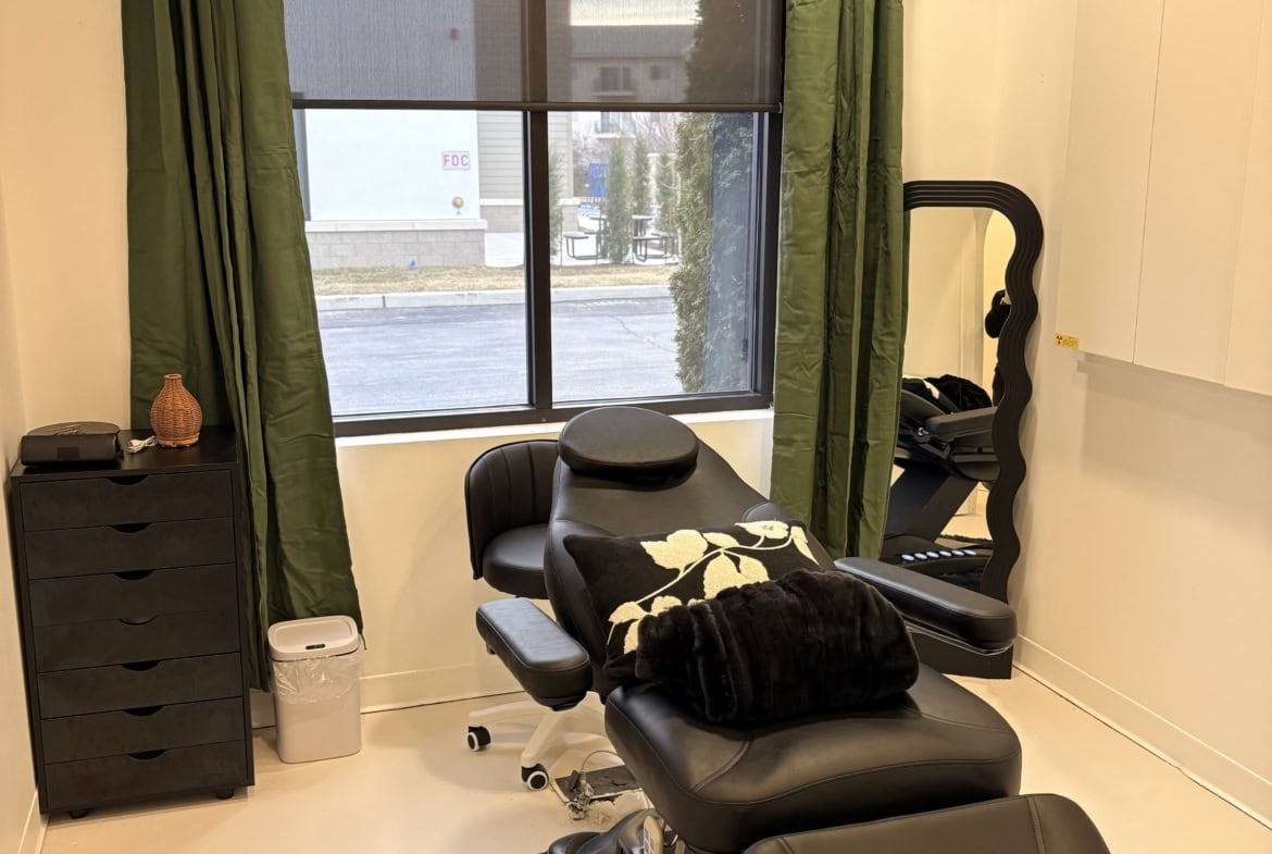 Relaxing salon treatment room with a comfortable chair and large window with green curtains.