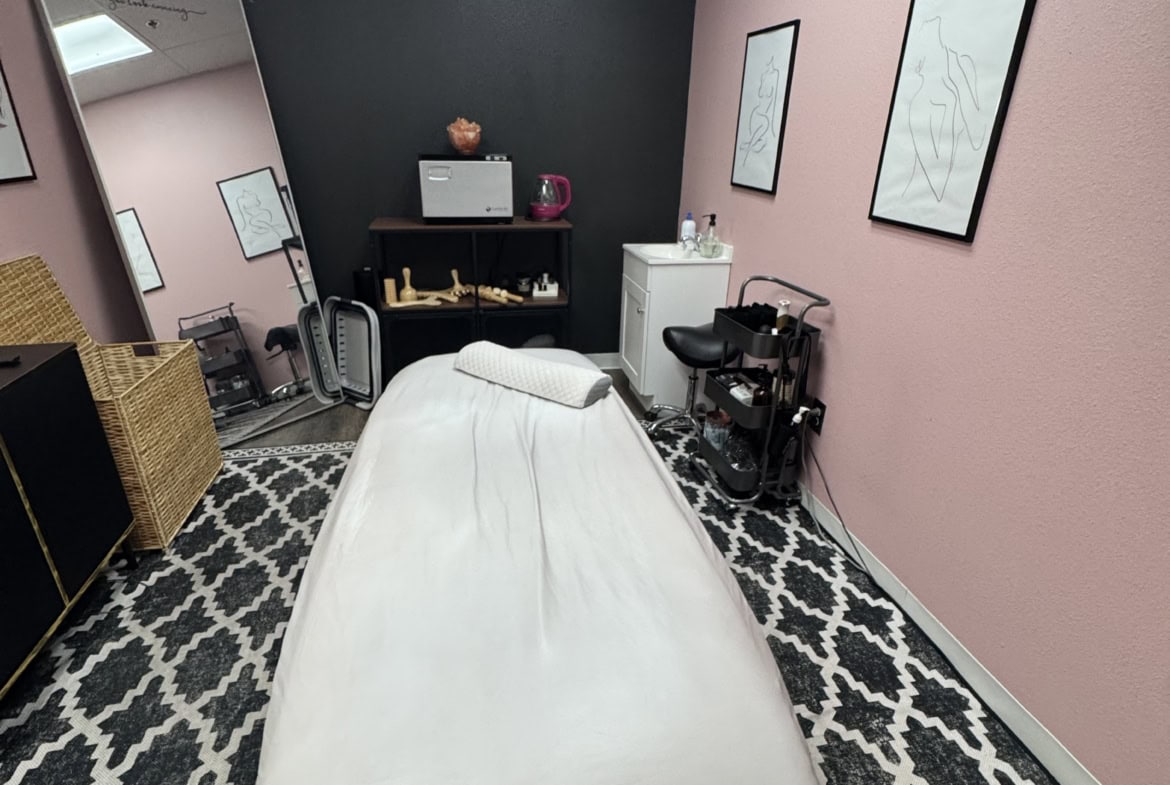 Massage table in a cozy salon room with pink and black walls, framed art, and relaxing decor.