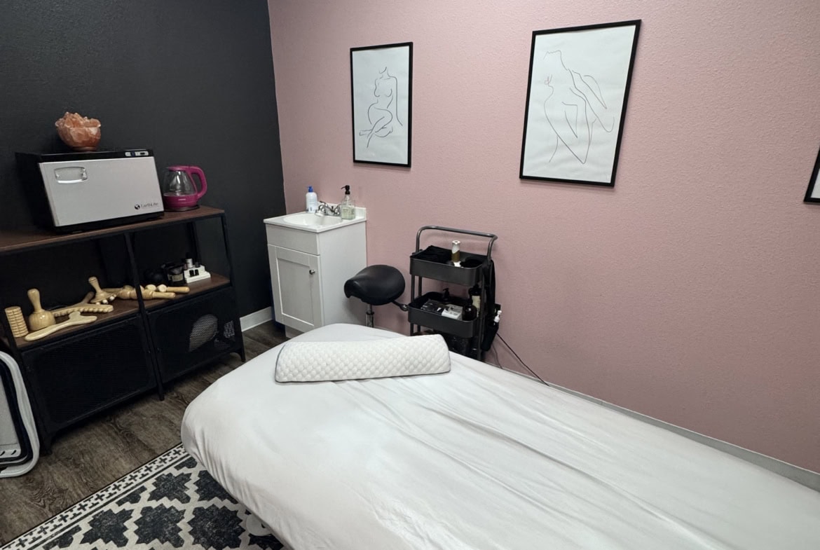 Massage therapy room with massage table, soft pink and black walls, and calming decor.