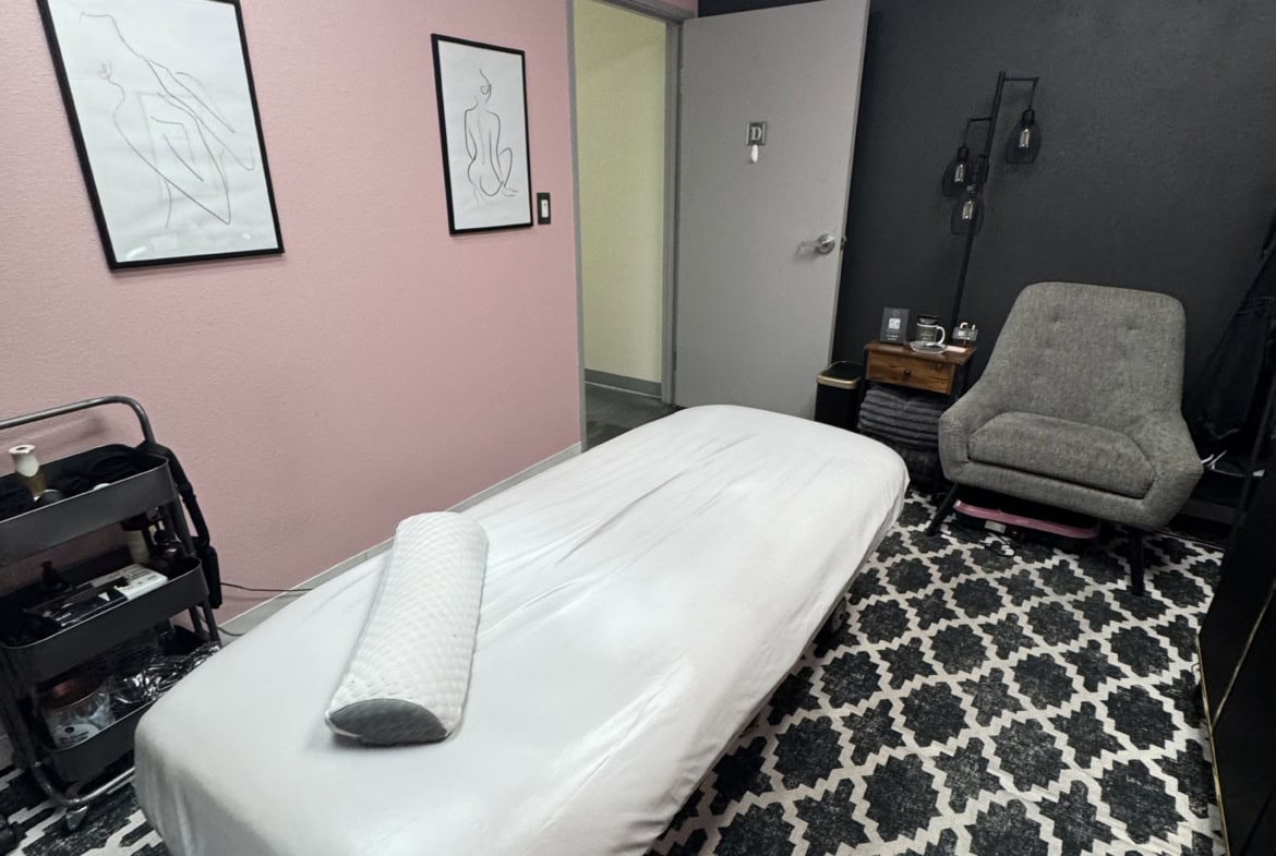 Massage therapy room with a massage table, cozy chair, and calming decor.