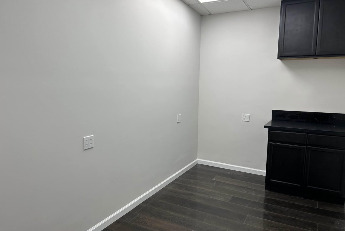 Empty salon corner with white walls and black cabinetry, ideal for salon rental or styling space.